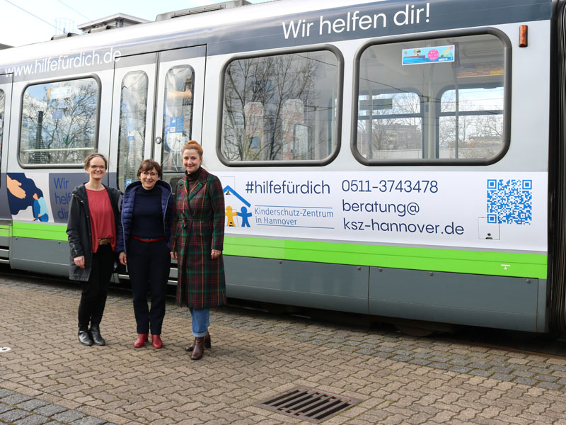 Dr. Anja Stiller, Dr. Chistine Arbogast und Denise Hain stehen vor der mit Bildern und Text beklebten Stadtbahn