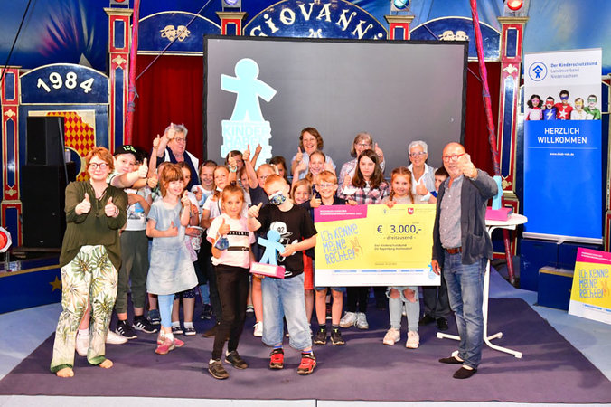 Kinder stehen mit der Ministerin und Johannes Schmidt in der Zirkusmanege und halten einen sehr großen Siegespreis-Scheck