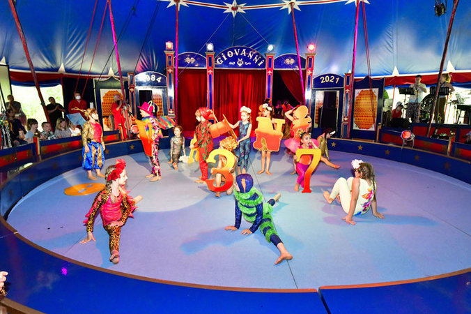 Kinder in bunten Fantasiekostümen turnen und tanzen in der Zirkusmanege