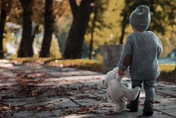 Kleines Kind (von hinten) mit Mütze und Teddibär unterwegs auf herbstlicher Allee, Foto: Elijah O'Donell | unsplash.com